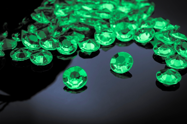 Emeralds scattered on a shiny surface with prominent emerald in the middle